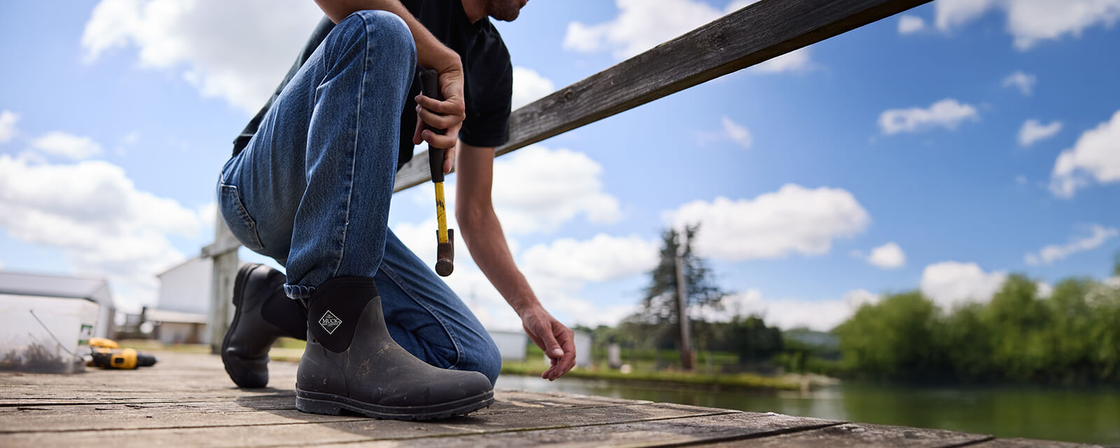 Ein Mann in Muck Boots Originals, der auf einem Knie niederkniet und einen Hammer in der rechten Hand hält.