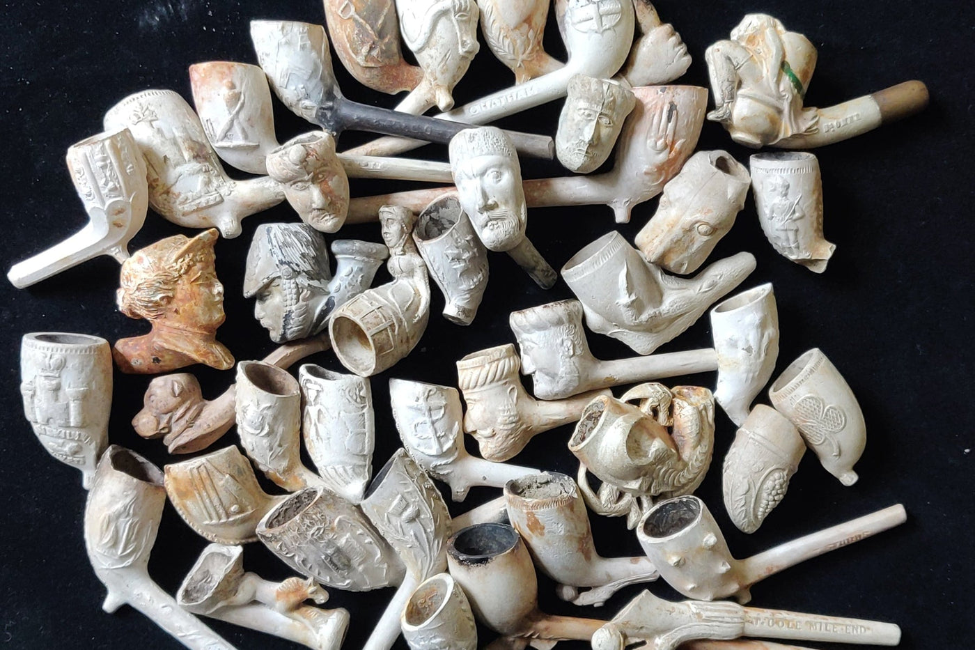 Eine Sammlung von Tonpfeifenköpfen aus dem 19. Jahrhundert auf schwarzem Hintergrund