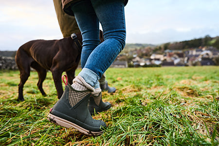 Person, die ein Paar Muck Boots Kurzstiefel trägt und durch Gras stapft