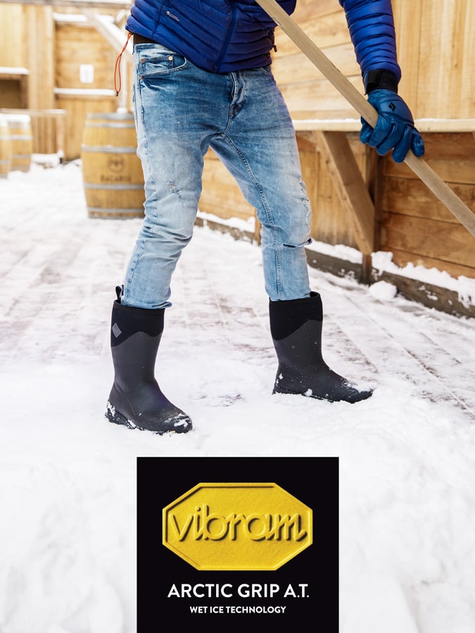 Nahaufnahme einer Person, die im Schnee steht und ein Paar Muck Boots trägt. Vibram-Logo auf der linken Seite