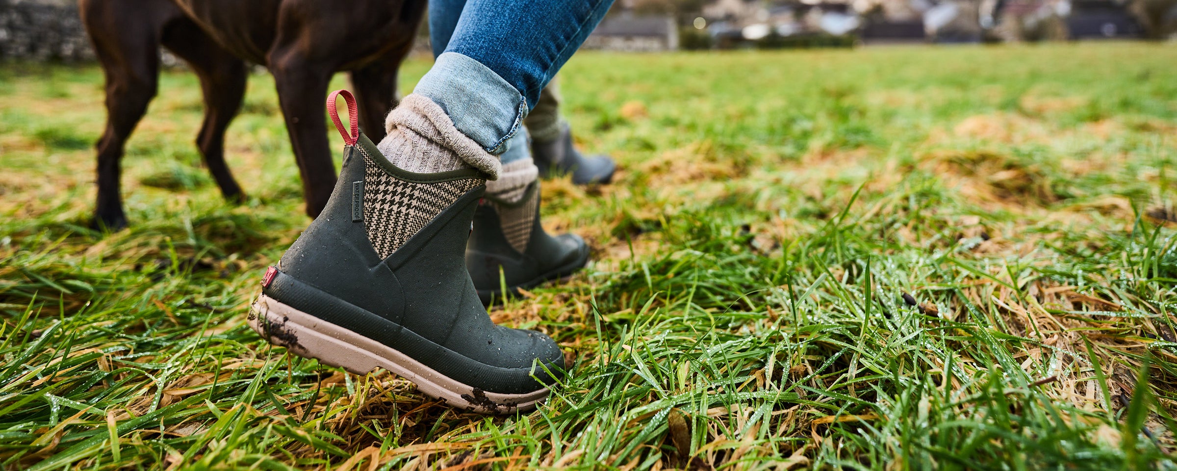 Person, die ein Paar Muck Boots Kurzstiefel trägt und durch Gras stapft