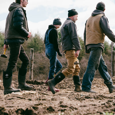 Mehrere Personen, die mit Muck Boots durch ein schlammiges Feld laufen