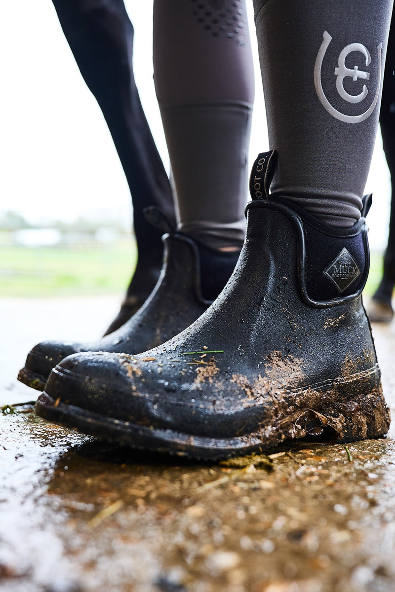 Nahaufnahme einer Person, die ein Paar mit Schlamm überzogene Muck Boots Unisex Wear Ankleboots trägt