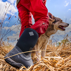 Person, die ein Paar Muck Boots trägt und mit einem Hund durch ein Ackerfeld geht