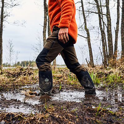 Mann, der in einem Paar Muck Boots durch schlammigen Boden läuft