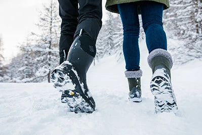 Ein Mann und eine Frau spazieren in Muck Boots Arctic Grip Gummistiefeln durch eine verschneite Landschaft.
